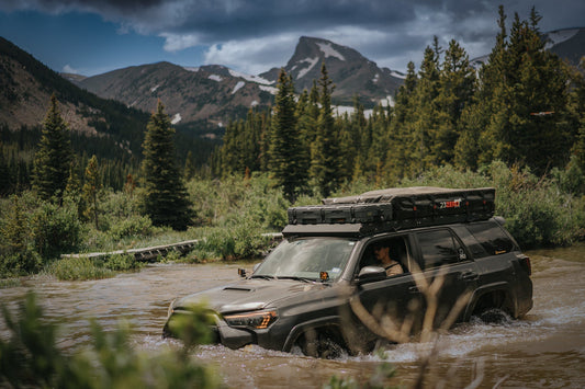 Gray 5th gen Toyota 4Runner with roof rack crossing a river with mountains