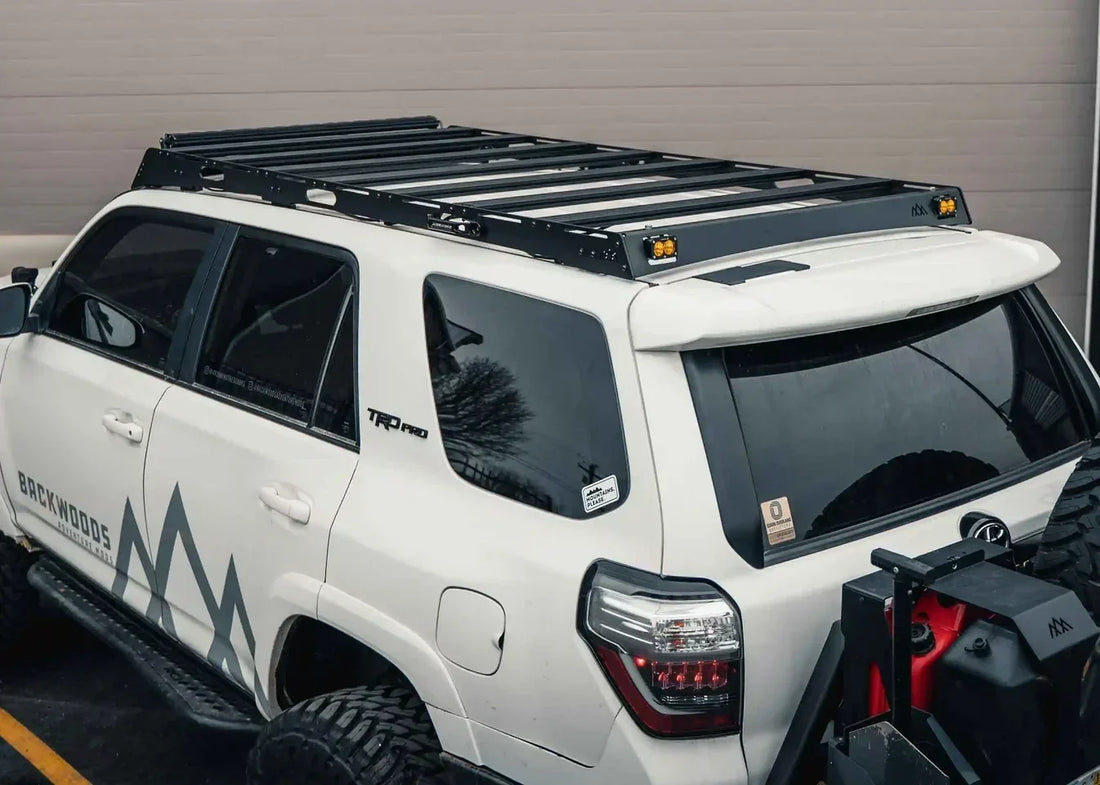 White 5th gen Toyota 4Runner with full-length black roof rack, rear view