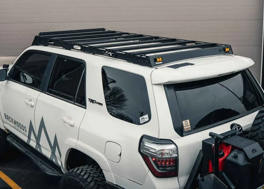 White 5th gen Toyota 4Runner with full-length black roof rack, rear view