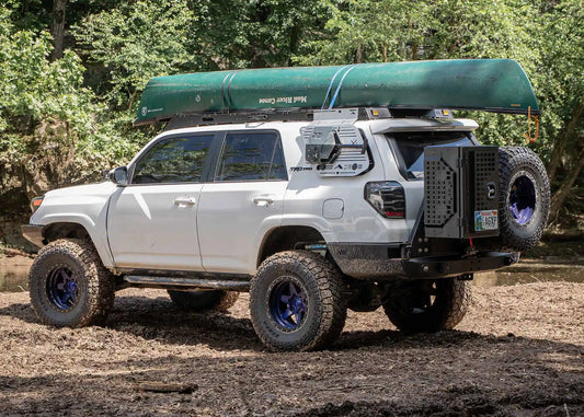 Silver 5th gen Toyota 4Runner with rooftop tent on a full-length roof rack among trees
