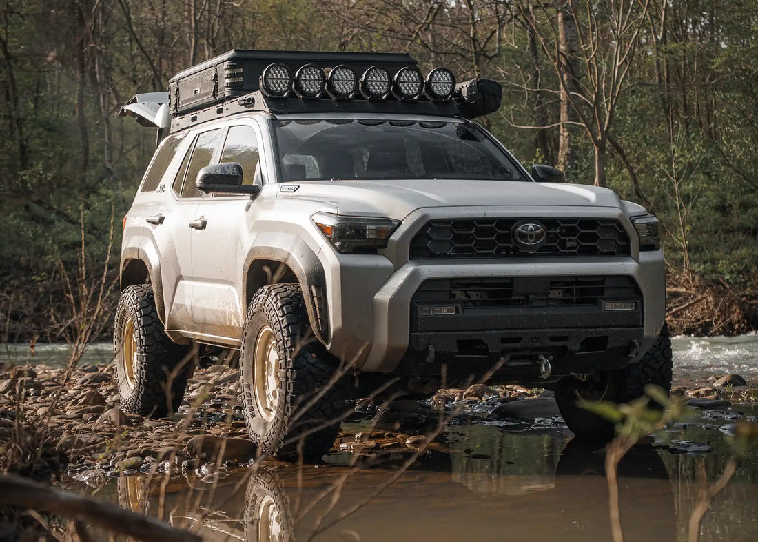 White 6th gen Toyota 4Runner with roof rack crossing a muddy trail